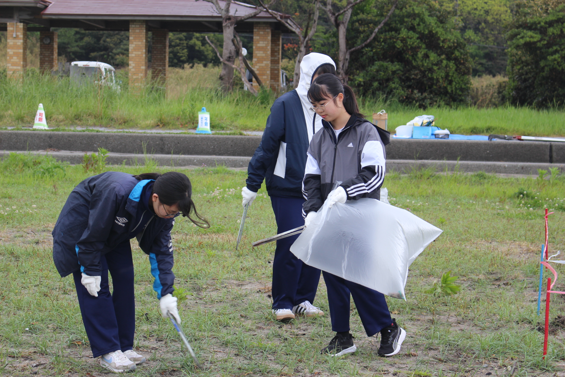 屋外で生徒たちがトングとゴミ袋を持ってごみ拾いをしている写真