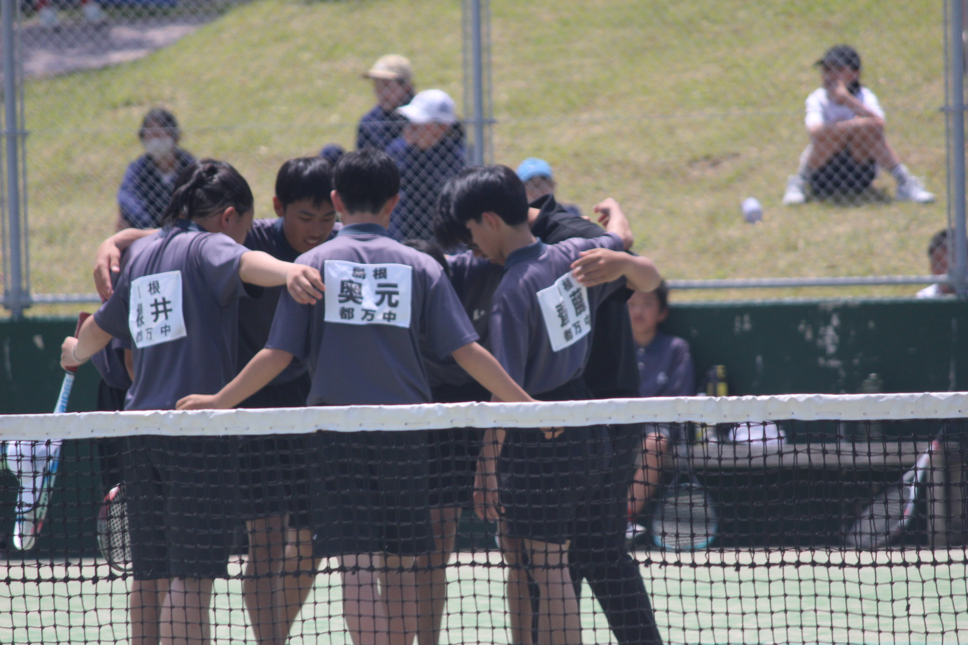 テニスコートの中で円陣を組む選手たちの写真