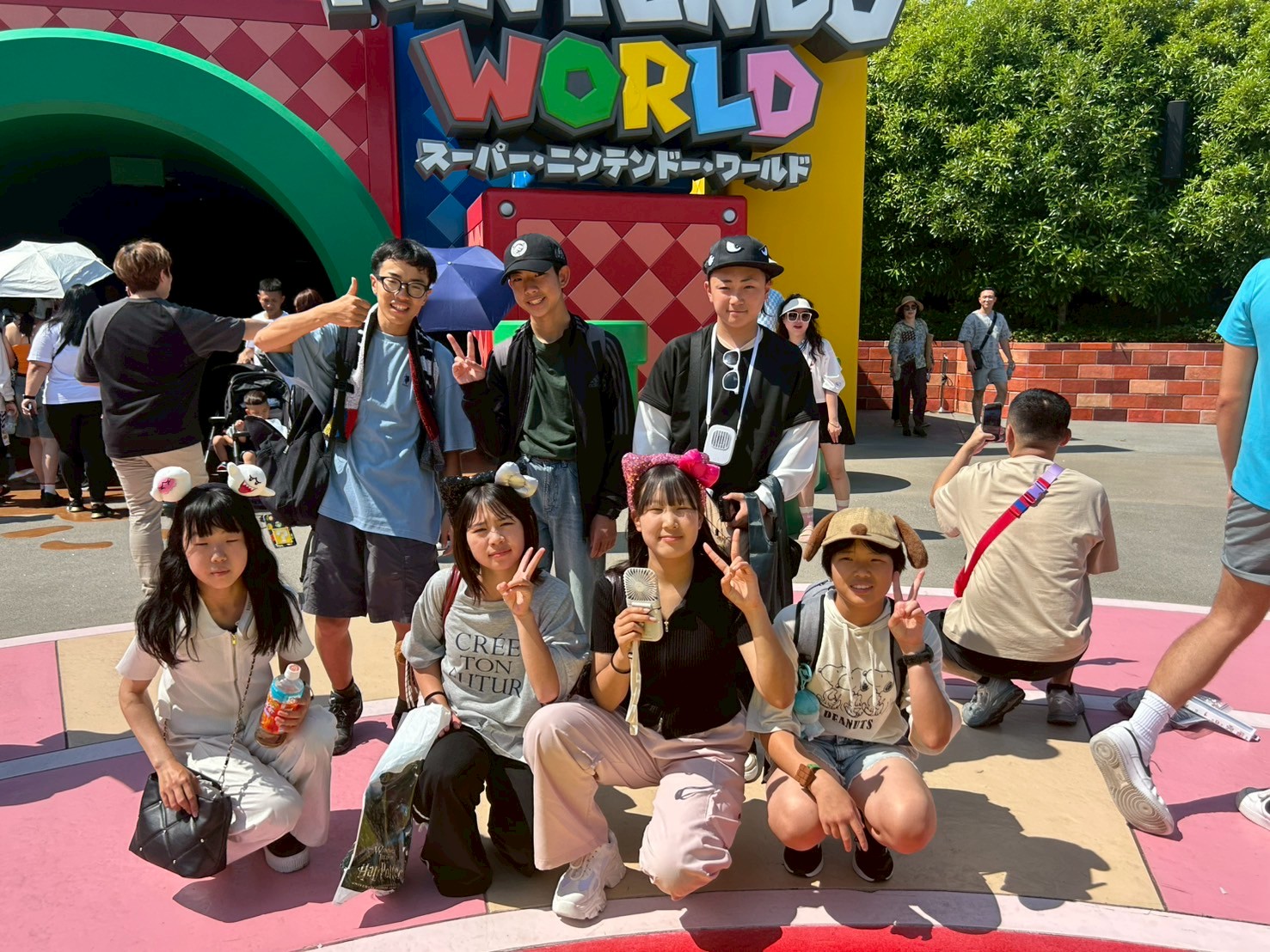 テーマパークの建物前で生徒たちが笑顔でポーズをとっている写真