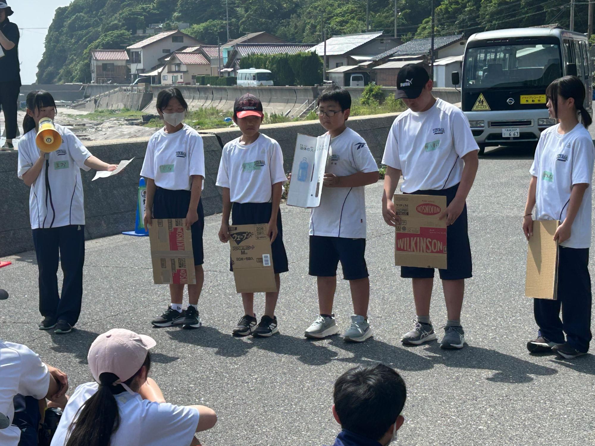 道路沿いで段ボールを持った生徒たちが説明をしている写真