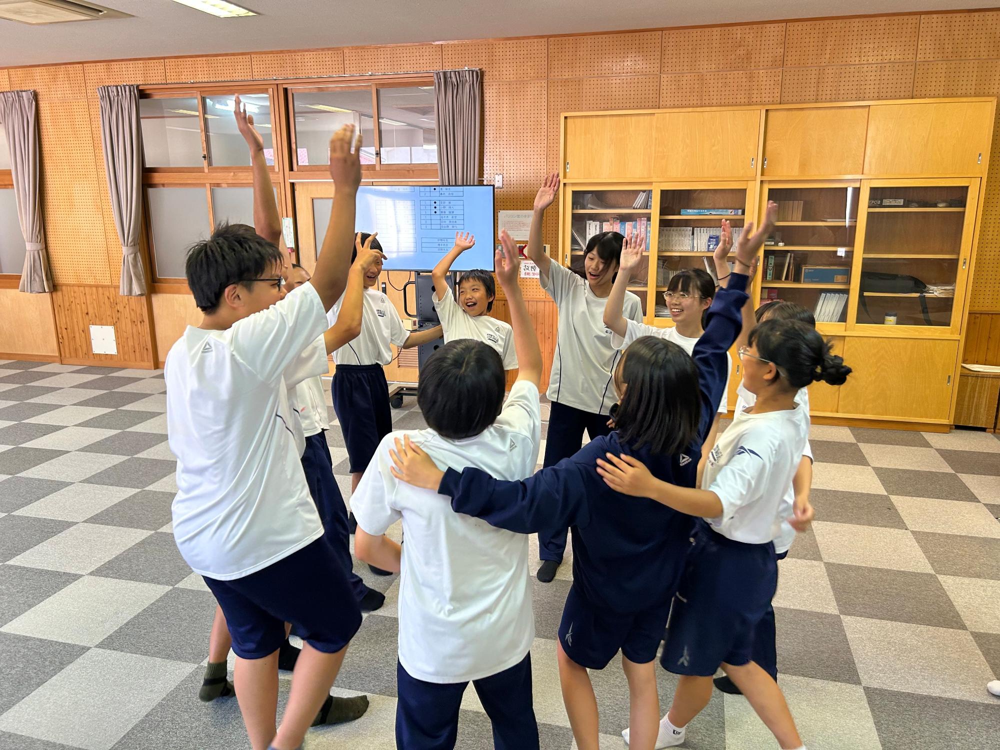 教室で生徒たちが円になって片手をあげて盛り上がっている写真