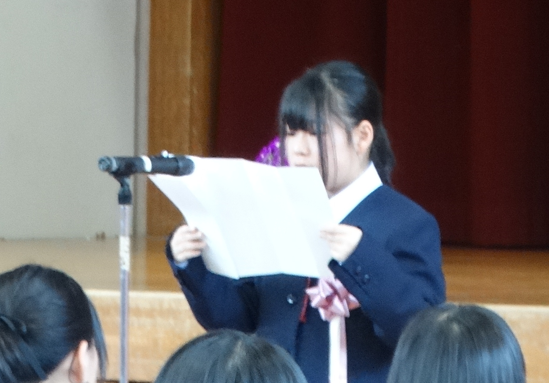 制服を着た女子生徒がマイクの前に立ち原稿を読み上げている写真