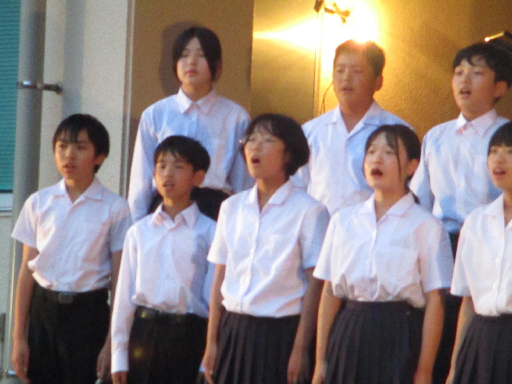 校舎前で生徒たちが並んで合唱をしている写真