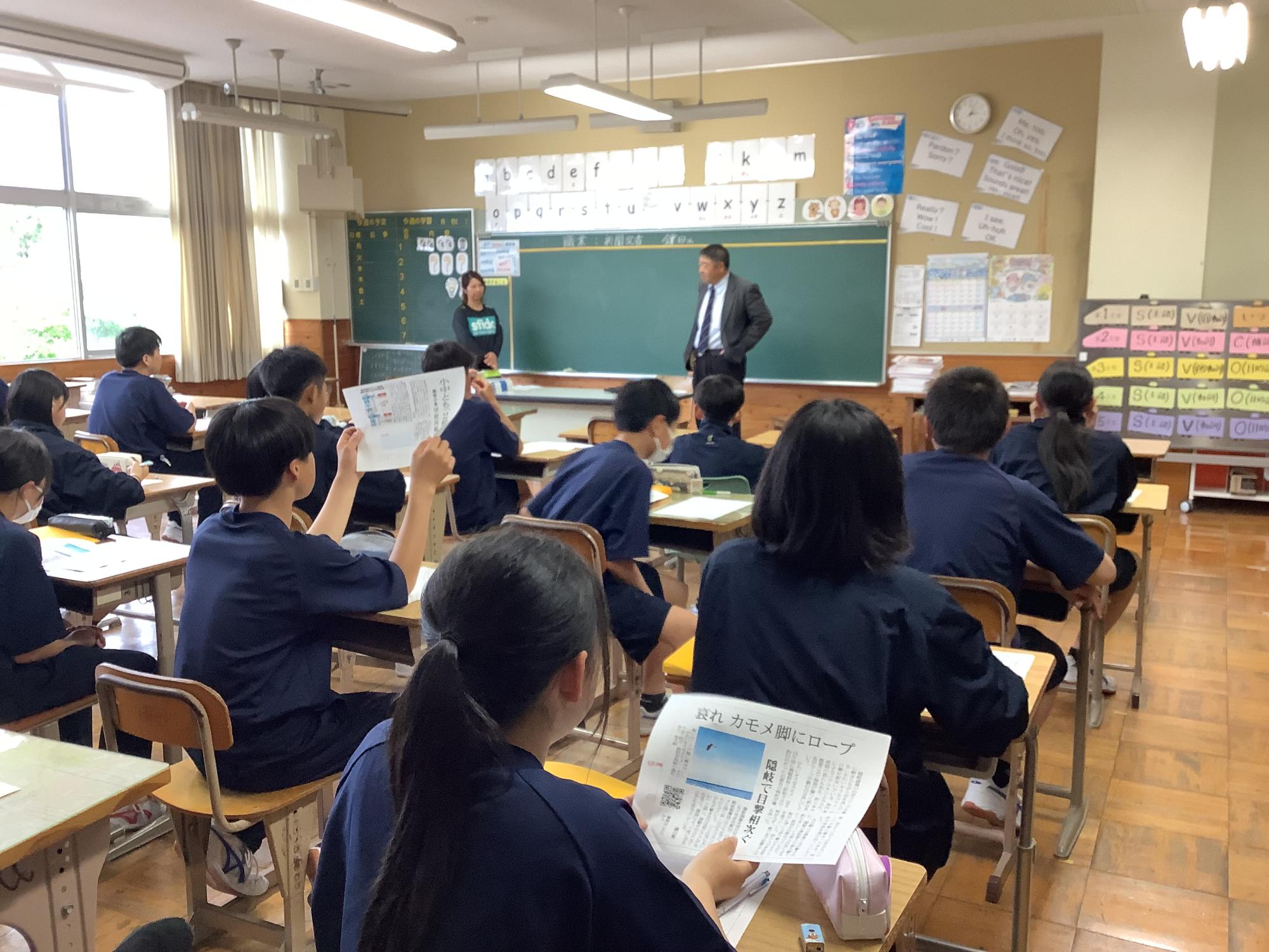 教室で生徒たちが先生の話を聞きながら授業を受けている写真