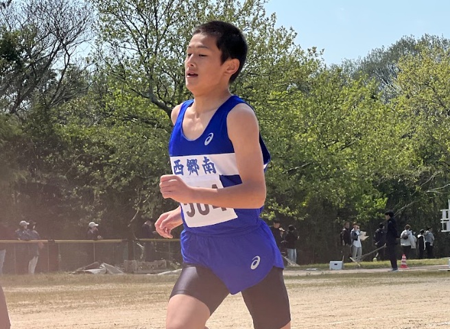 陸上競技のユニフォームを着た男子生徒がグラウンドで力強く走る写真