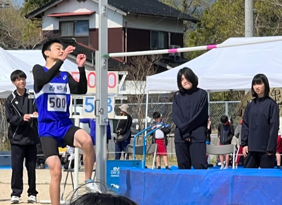 グラウンドで男子生徒が走り高跳びに挑戦している写真