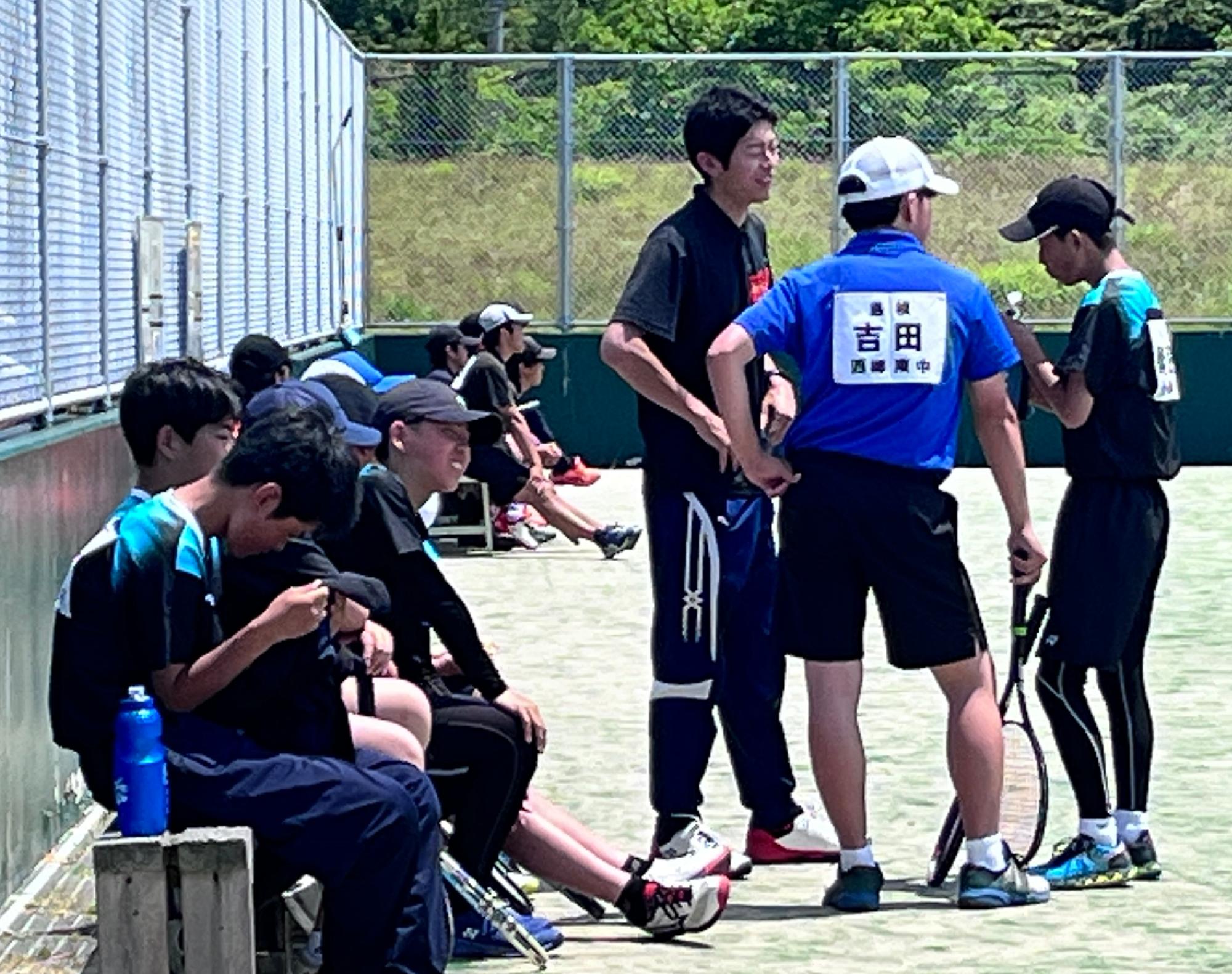 テニスコートで男子生徒たちが試合の合間に話し合っている写真