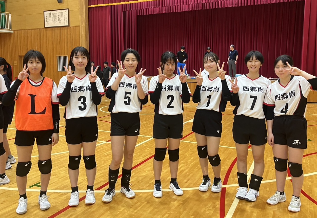 体育館で女子バレーボール部の生徒たちが一列に並んで両手でピースのポーズをとっている写真