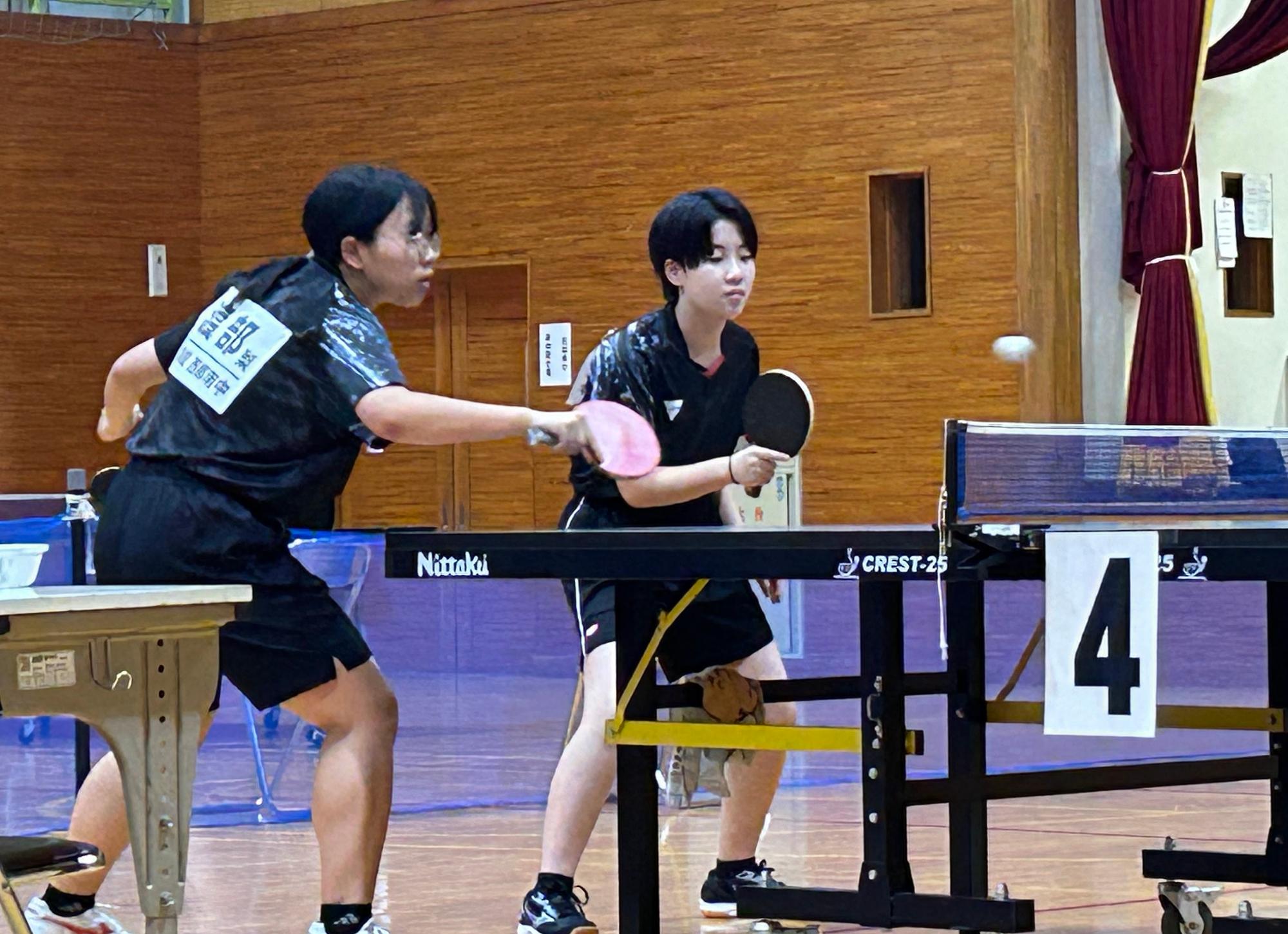 体育館で女子生徒が二人組で卓球の試合をしている写真