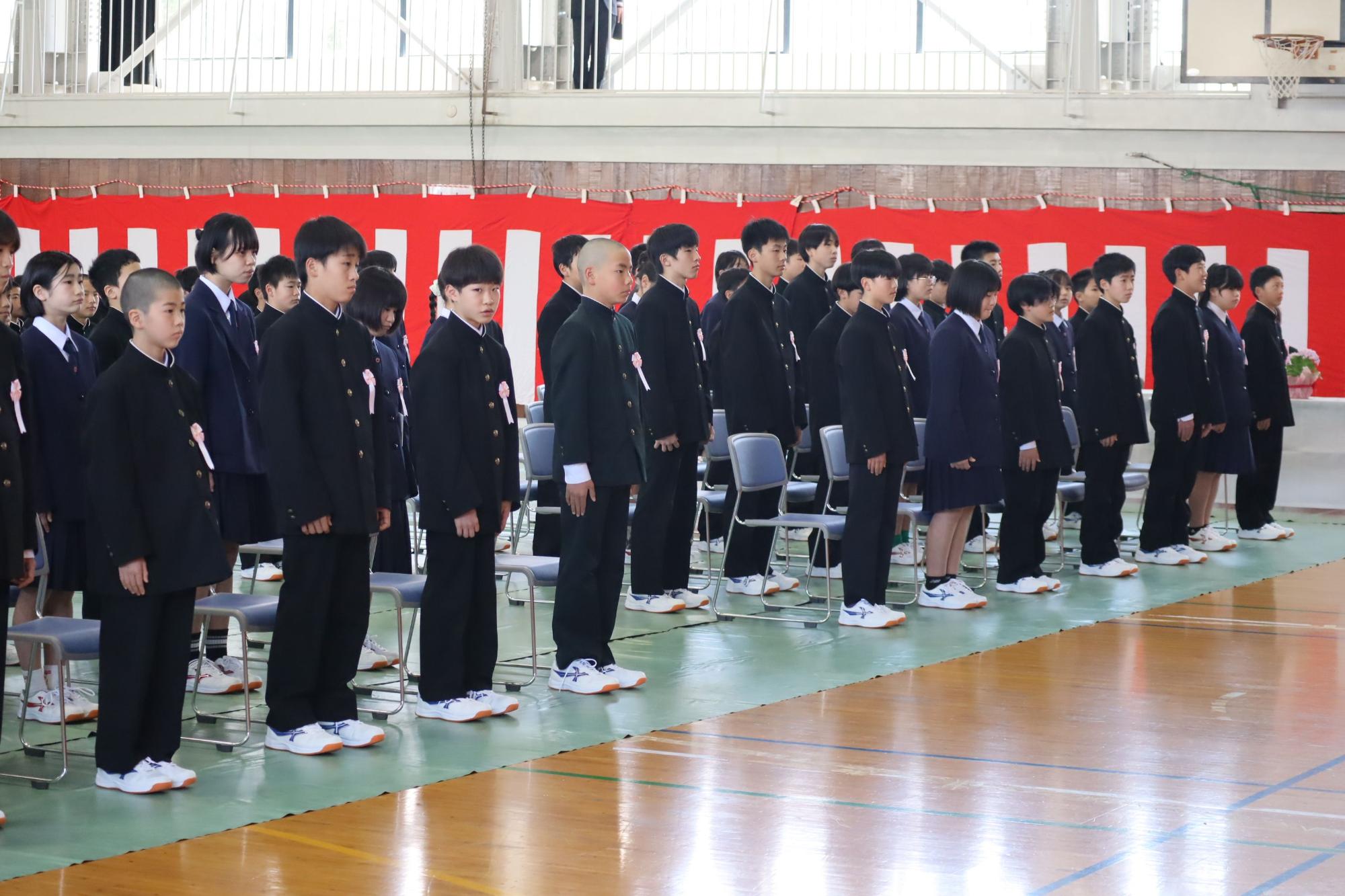 体育館で制服姿の生徒たちが起立している写真