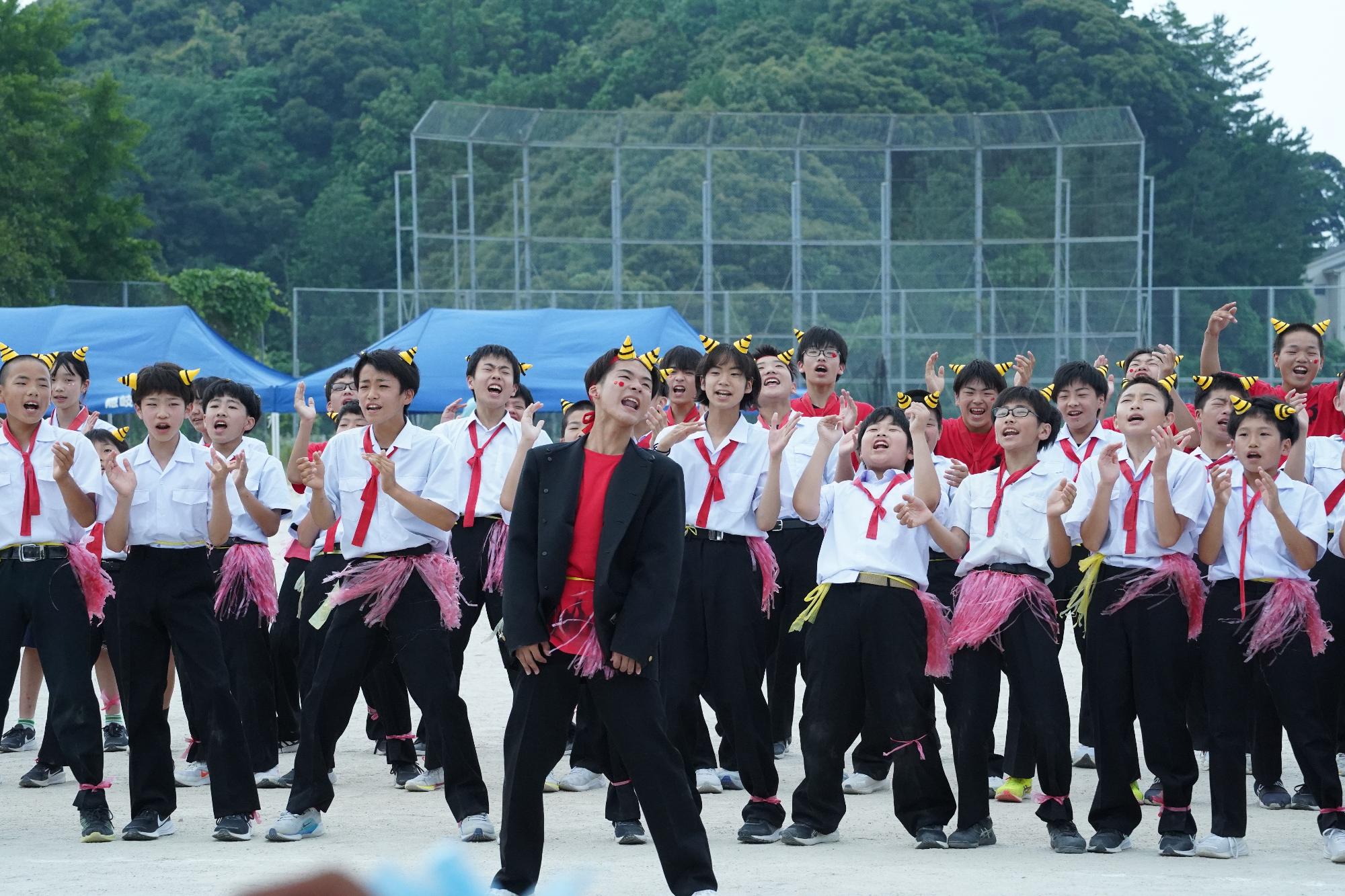 校庭で赤い鉢巻を首に巻いた白Tシャツの生徒たちがパフォーマンスをしている写真