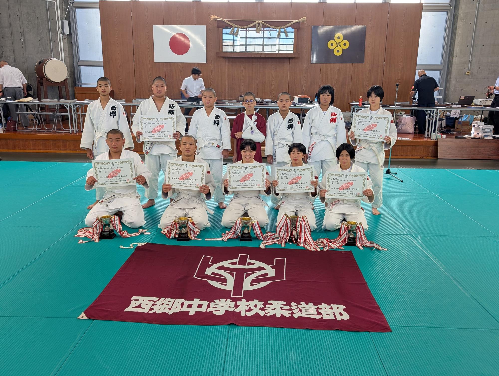 武道場で柔道部の生徒たちが賞状を持って並んでいる写真