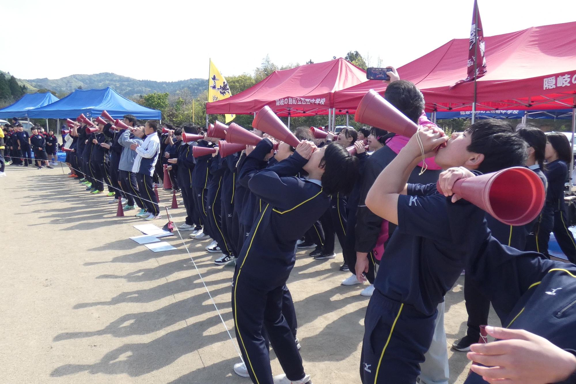 グラウンドで生徒たちがメガホンを使って声援を送っている写真