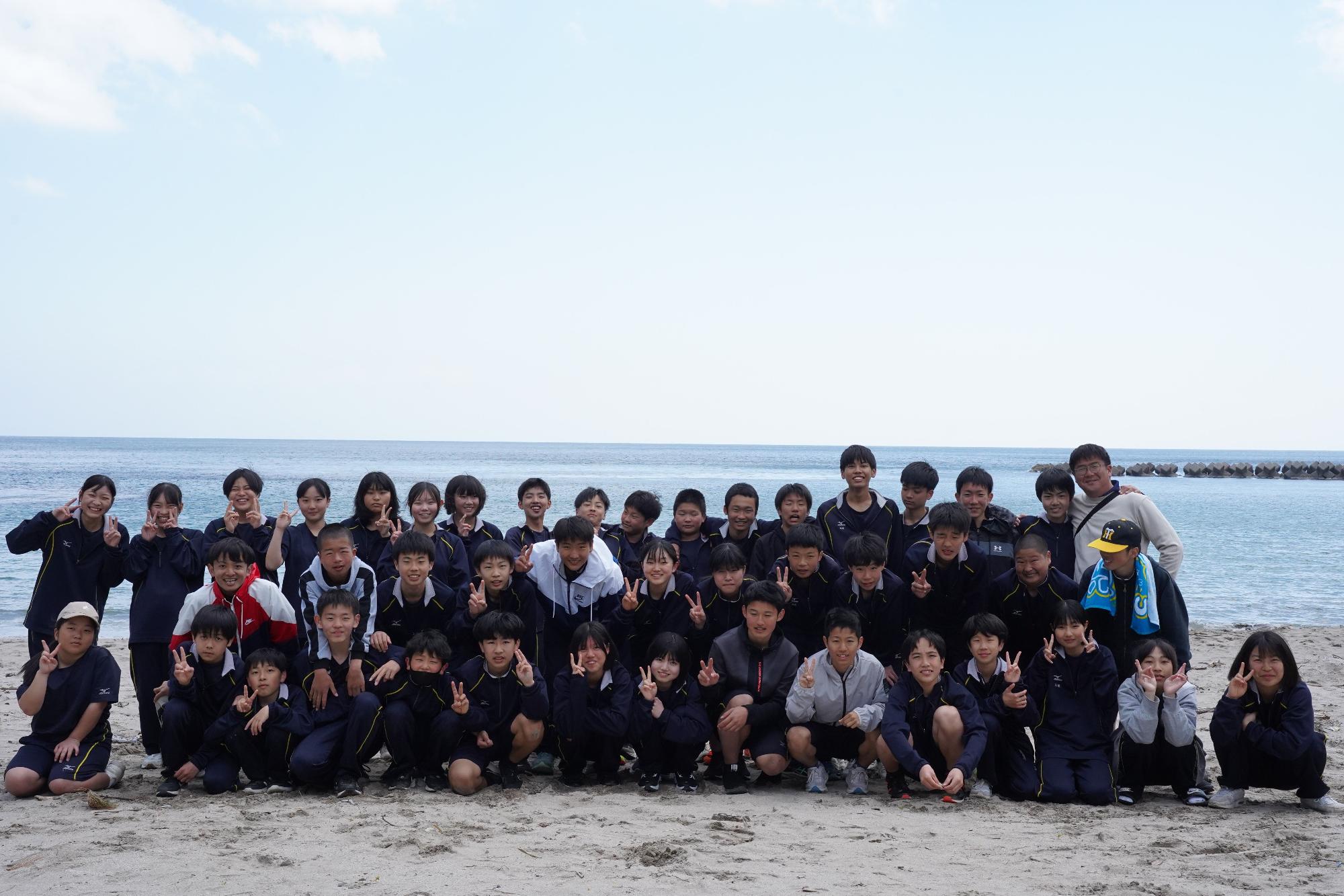 海辺でジャージ姿の生徒たちが集合して記念撮影をしている写真
