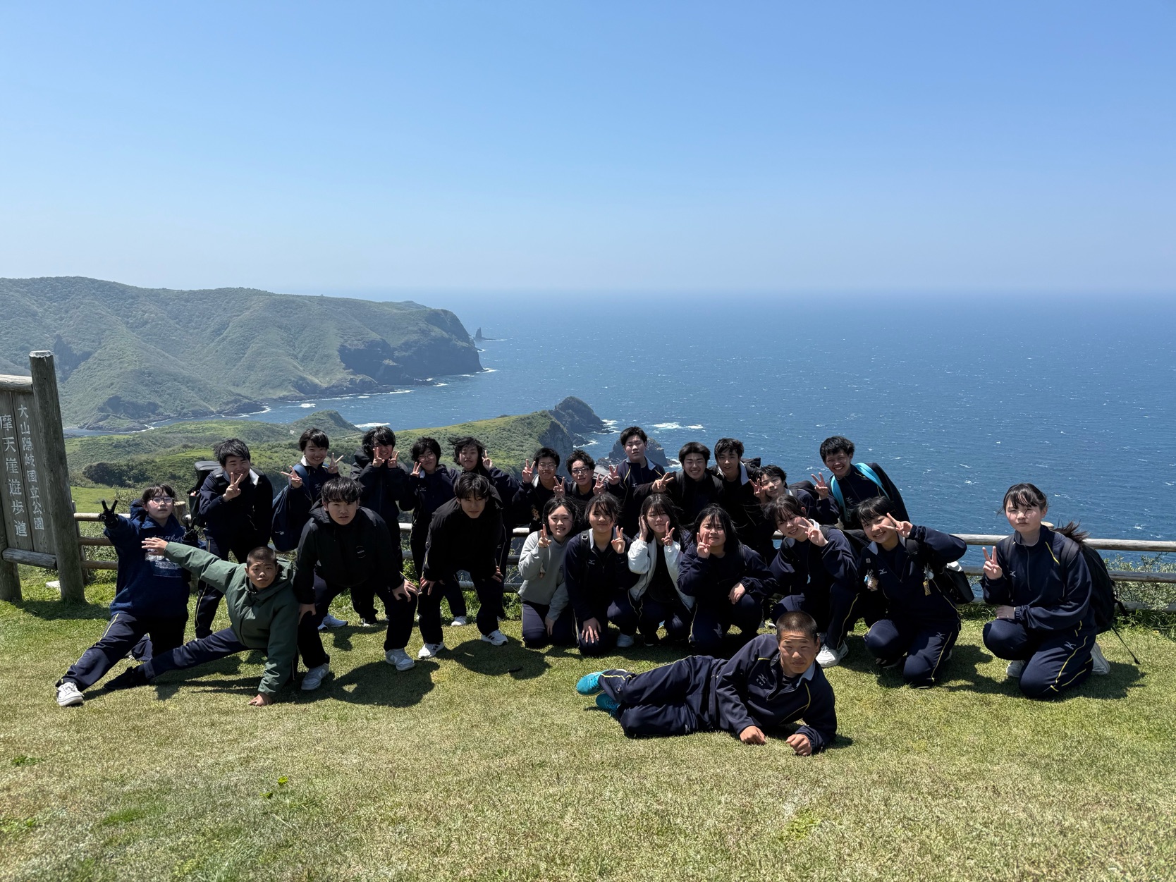 岬に居る生徒たちが海を背景にポーズをとっている写真