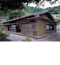 森を背景にした、石置き屋根の佐々木家住宅の写真