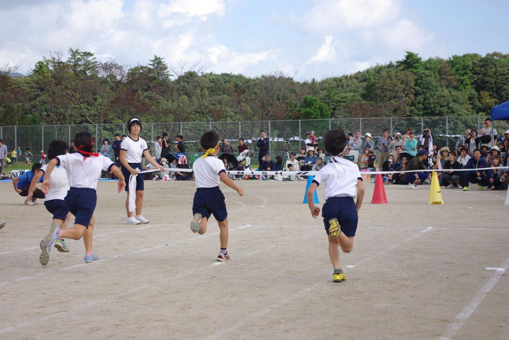 校庭で児童がゴールテープに向かって走っている写真