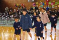 体育館で年上の児童が年下の児童の手を引いて歩いている写真