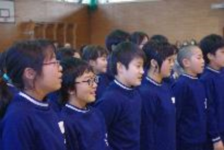 体育館で子どもたちが横に並び前を向いて歌っている写真