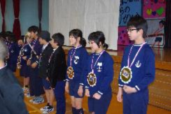 生徒たちが首に大きな飾りを下げ並んで立っている写真