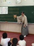 和服を着た講師の先生が児童たちに黒板の前で面を見せている写真