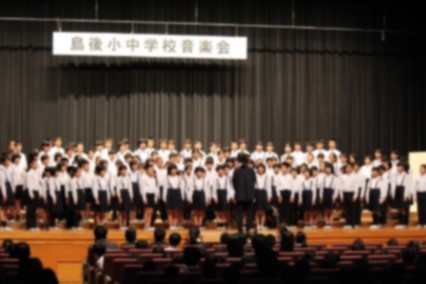 児童たちがお揃いの服を着てステージに並び合唱をしている写真