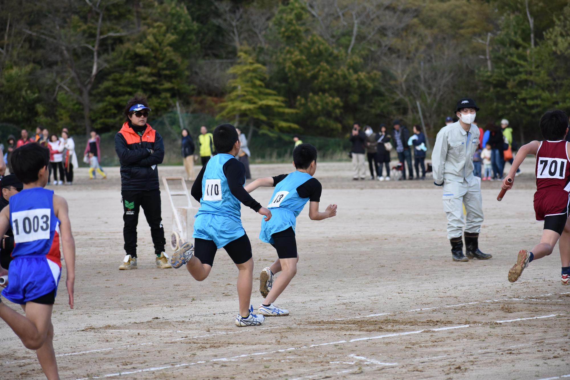 ゼッケンをつけたリレーの選手がバトンを渡している写真