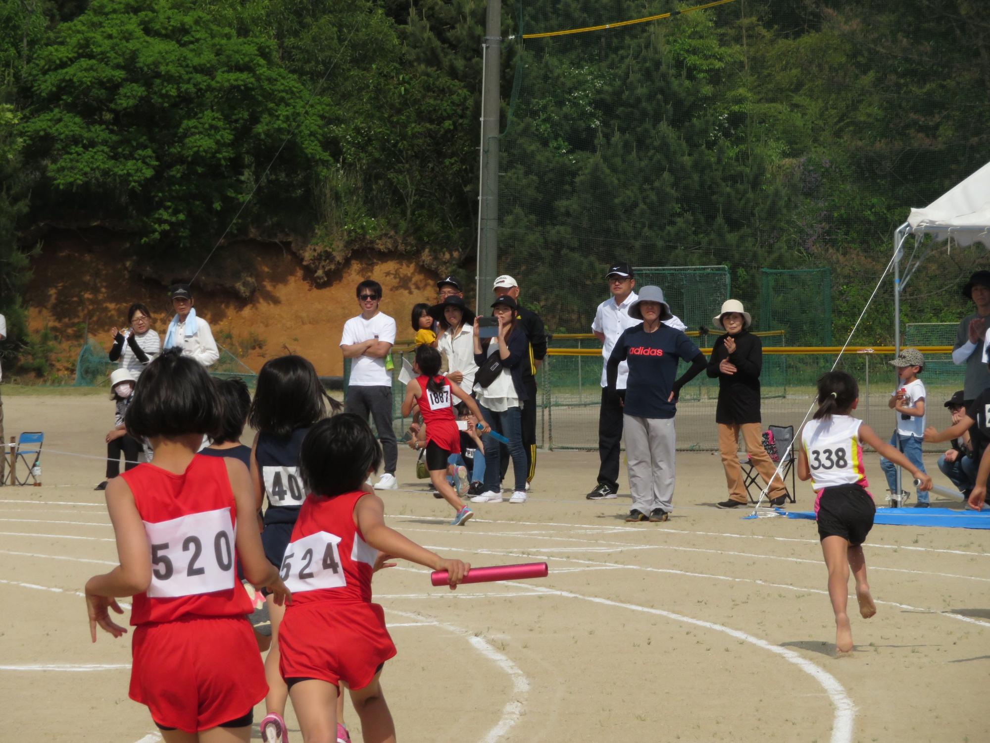 ユニフォームで走っている児童たちがバトンを受け渡している写真