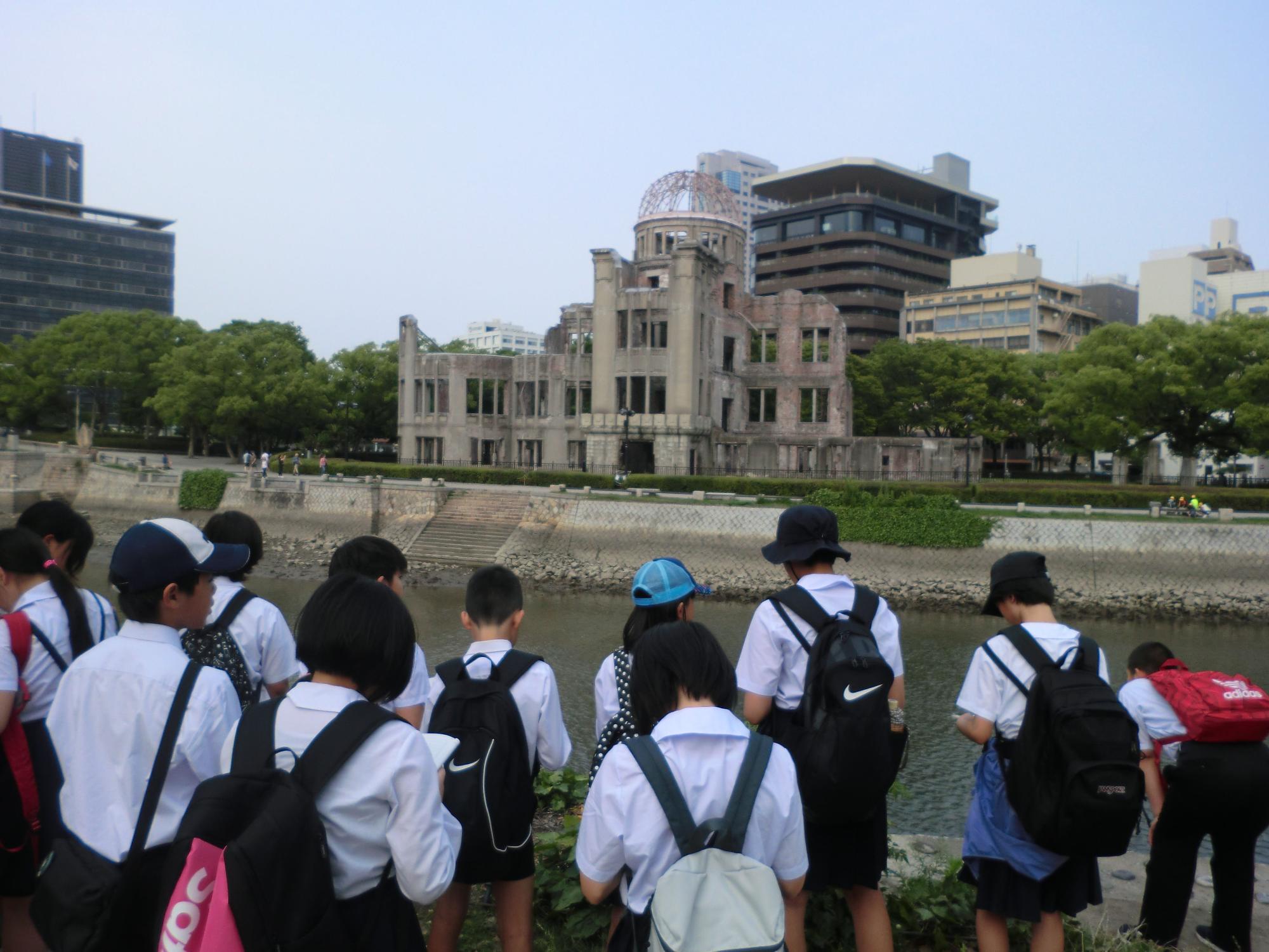 川越しに原爆ドームを見ながらメモを取っている児童たちの写真