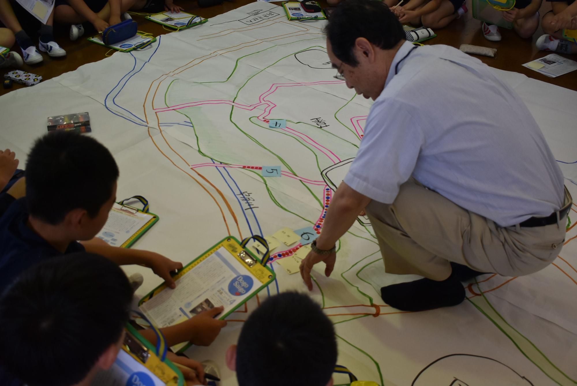 床に敷かれた地図を囲んで座っている児童たちの写真