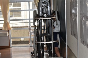 壁際に折りたたみ椅子のようなものが置いてありその後ろに1人の児童が隠れている写真