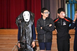 複数の児童が体育館のステージ前で仮装やユニークな眼鏡を身につけて並んでいる写真