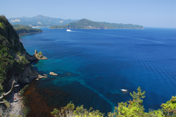 海辺の崖の上から真っ青な海を見下ろして遠目に島が見えている写真