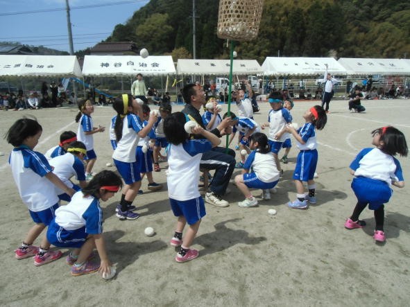 かごを支える男性のまわりで、児童たちが玉を投げている玉入れの写真