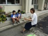 屋外で先生が児童に本を読み聞かせしている写真