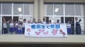校舎前で児童たちが完成したウルトラマラソンの応援幕を持っている写真