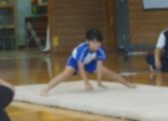 体育館で児童がマットの上で開脚前転に挑戦している写真