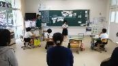 教室で児童が前に立ち発表しているのを他児童や保護者が見ている写真