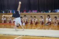 体育館でマットの上で側転している児童を他児童が見ている写真