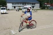 安全教室で自転車に乗る児童が校庭を走っている写真