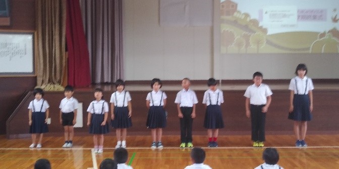 学年代表の児童が体育館のステージ前に並んで発表している写真