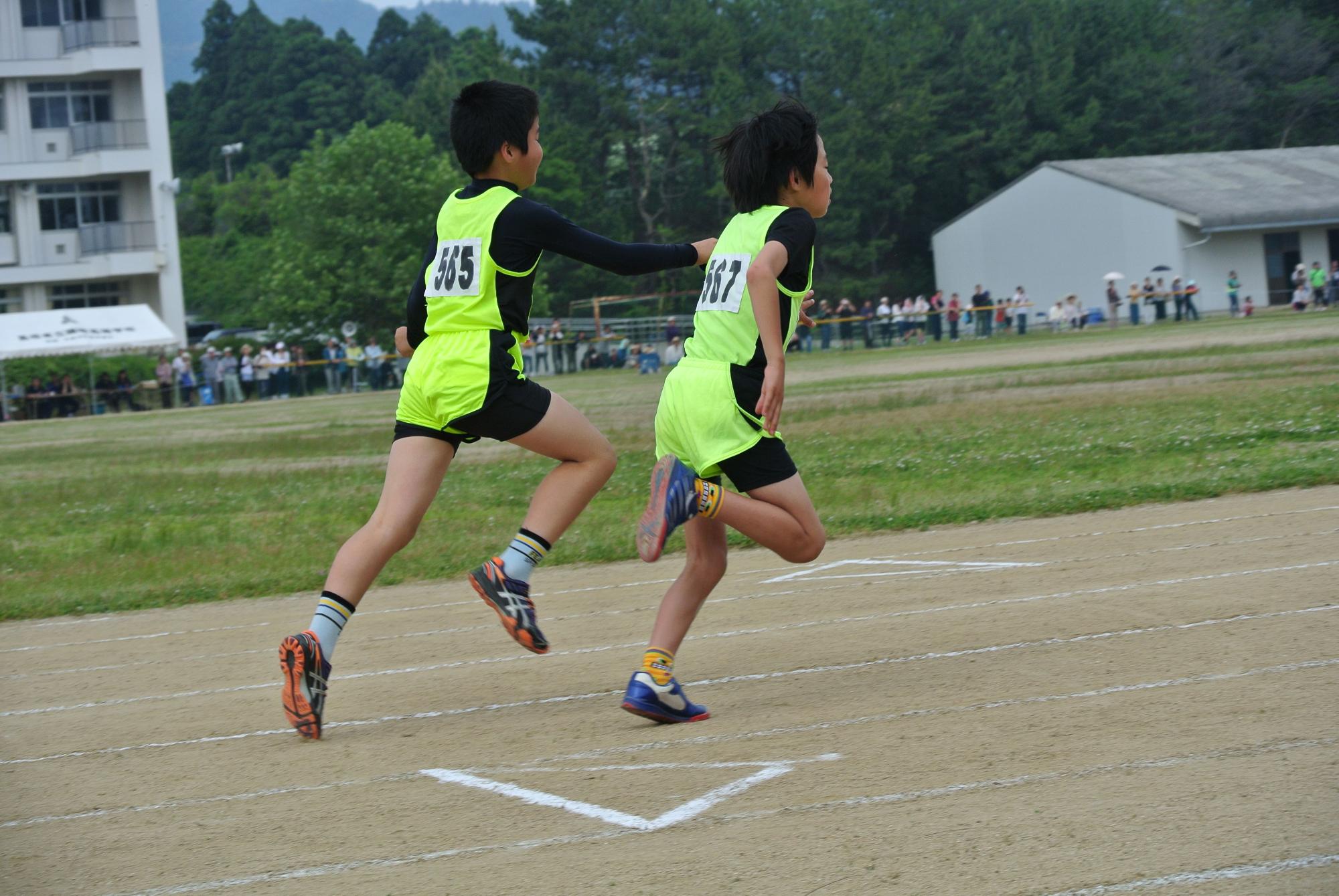 グラウンドで2人のユニフォーム姿の児童が走っている写真