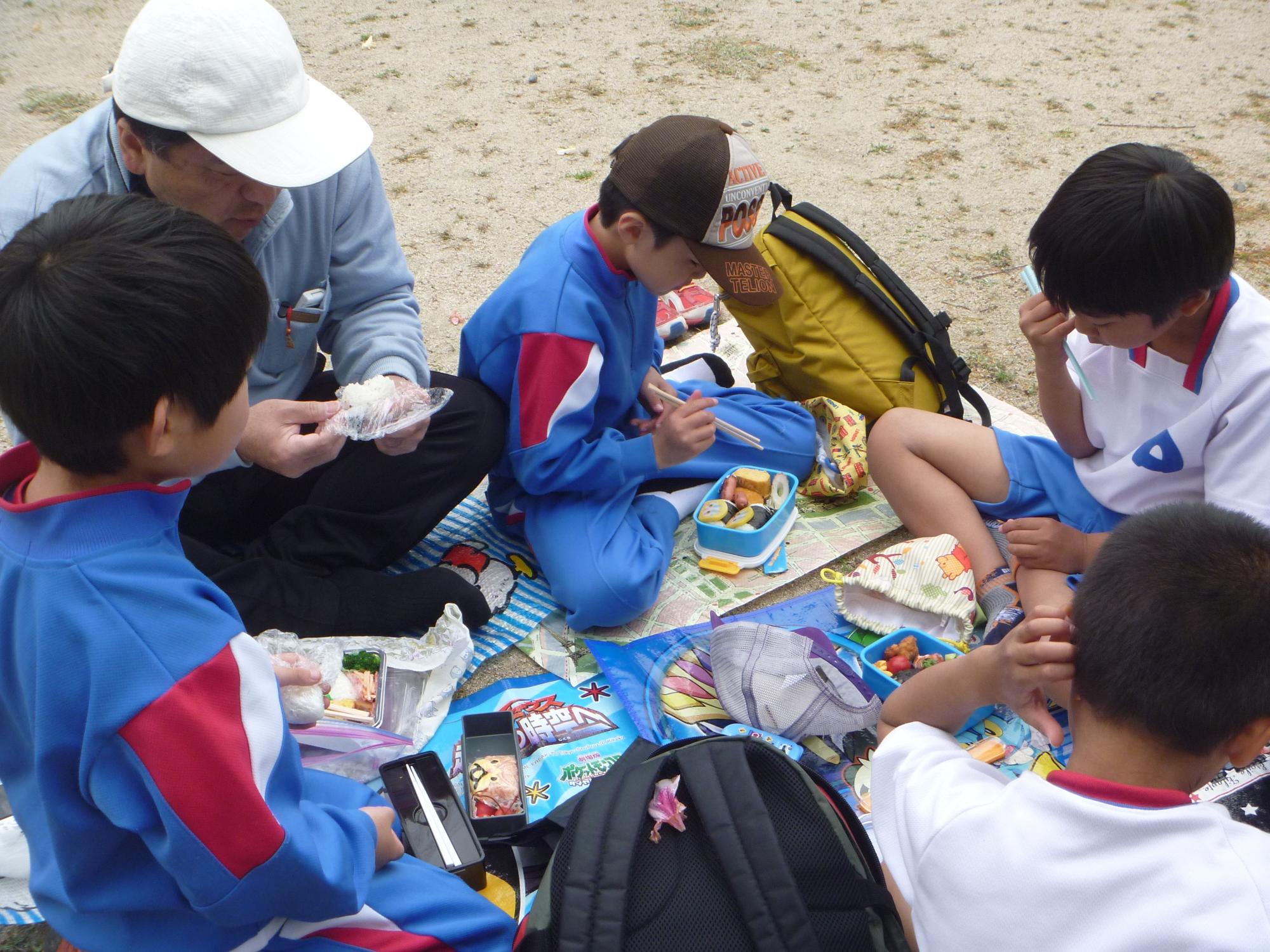 レジャーシートの上で男性と男子児童がお弁当を食べている写真