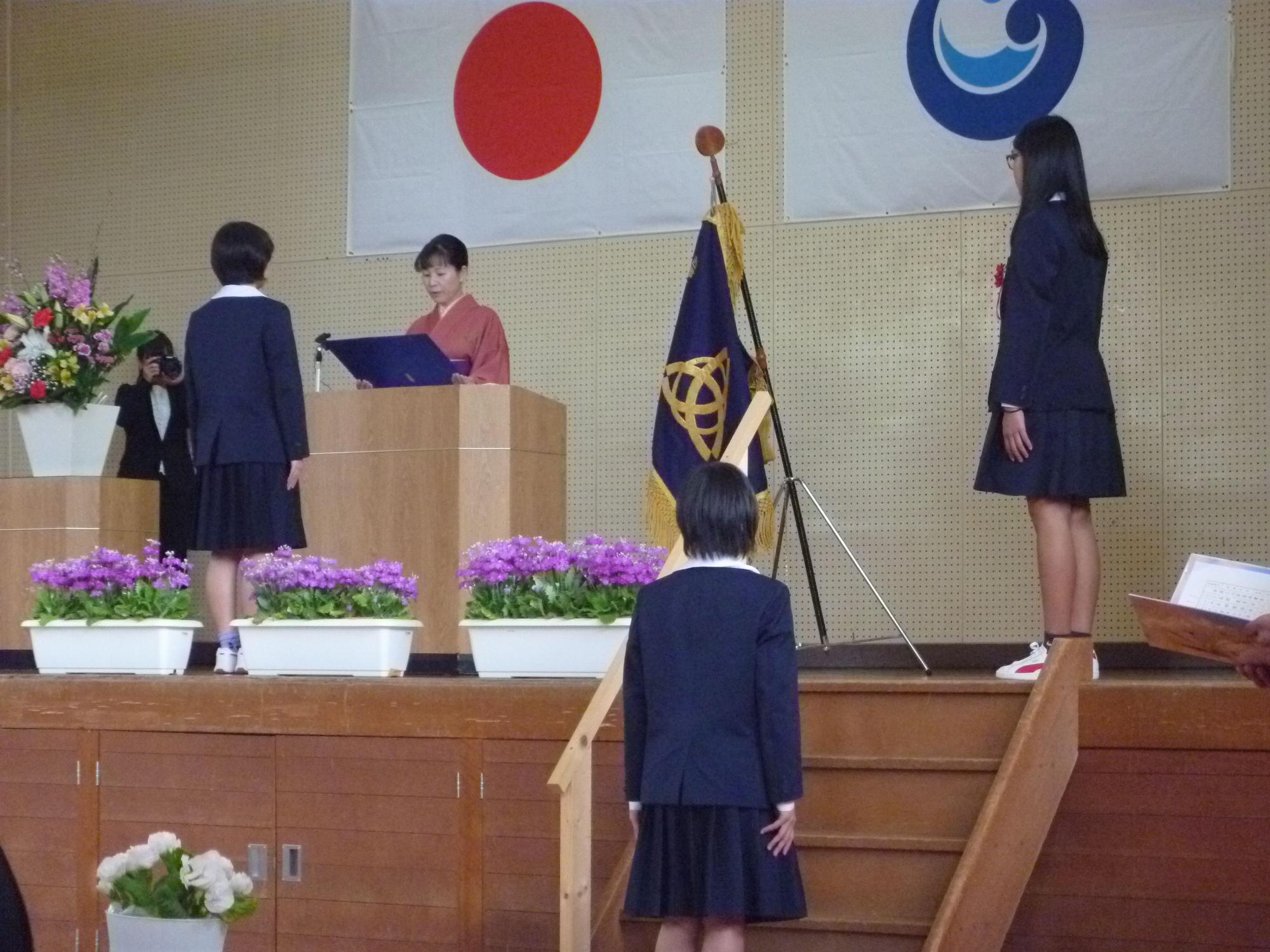 体育館で卒業生が一人ずつ卒業証書を受け取っている写真