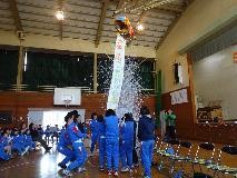 体育館の天井に吊るされたくす玉を割ってお祝いする児童たちの写真