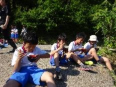 屋外で児童たちが座り、器を手にして豚汁を食べている写真