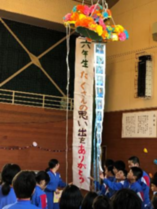 体育館の中で児童たちが割られた手作りくす玉を見上げている写真