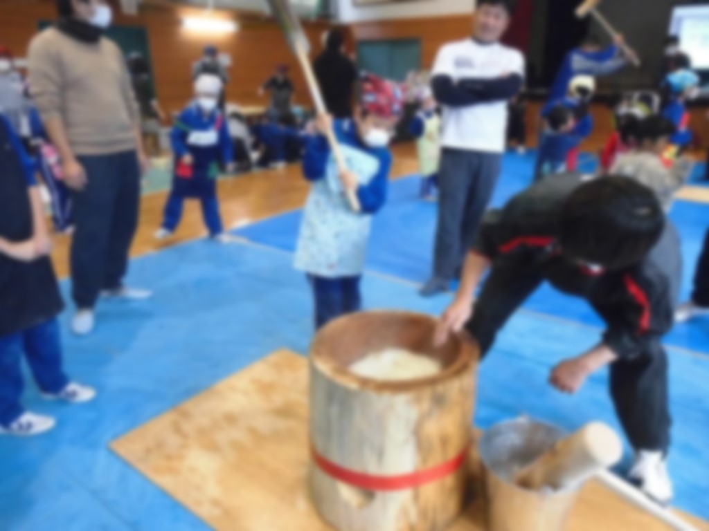 杵を持った児童と餅をこねている大人の写真