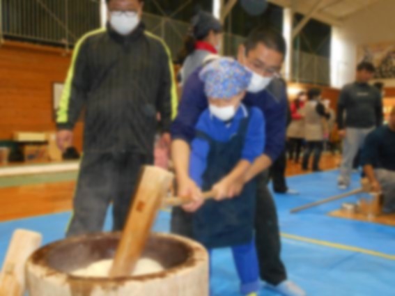 児童が大人に手伝ってもらいながら杵で餅をついている写真