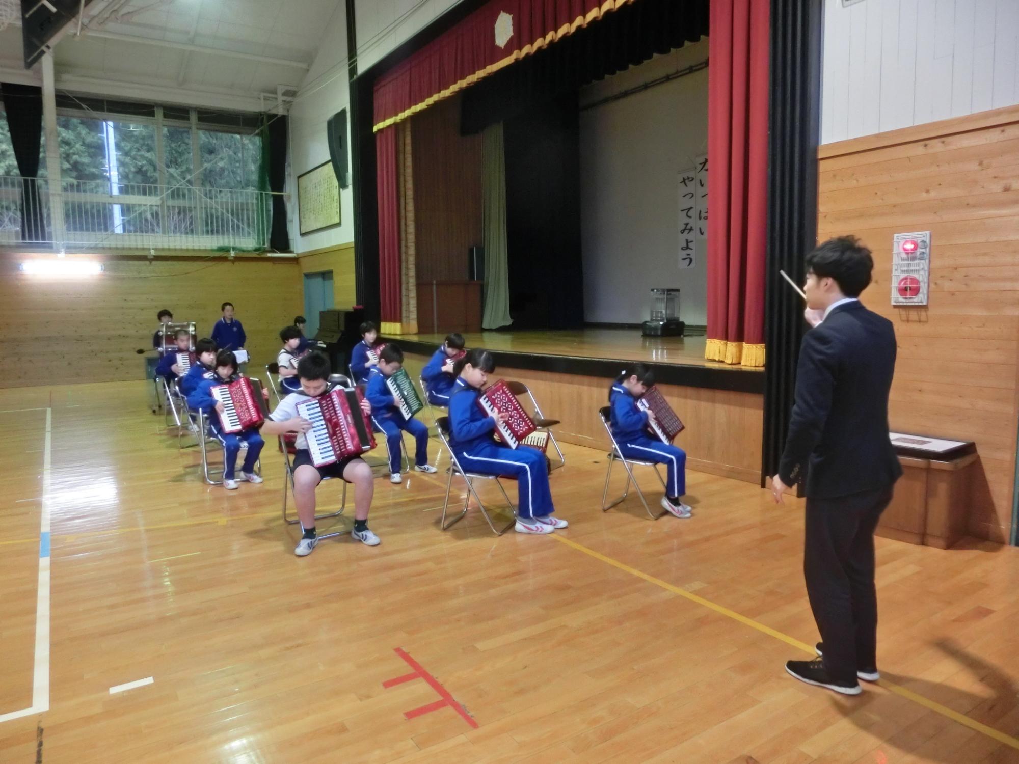 体育館で椅子に座って校歌を演奏している児童たちの写真